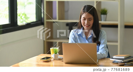 A woman is using a computer laptop that putting on a wooden working desk. A woman is using a computer laptop that putting on a wooden working desk. 77681689