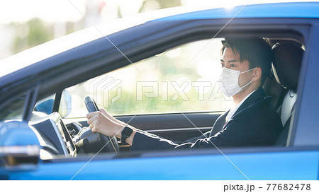 マスクをつけて車を運転するスーツの男性 77682478