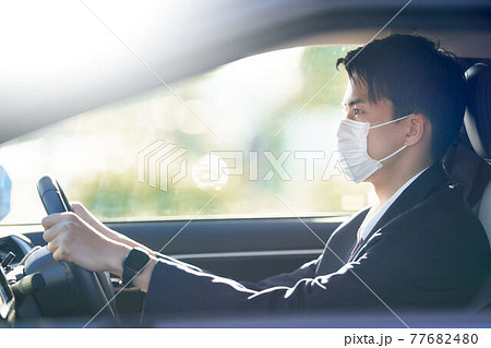 マスクをつけて車を運転するスーツの男性 77682480
