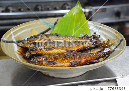 寿司屋のカウンターで、大皿に盛り付けられた丸ごと一尾の鮎の甘露煮。 77683343