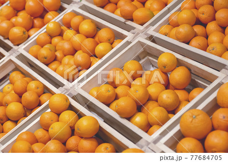 Oranges on the background market. Fresh oranges for juice in wooden boxes on the counter in the fruit and vegetable market Oranges on the background market. Fresh oranges for juice in wooden boxes on the counter in the fruit and vegetable market 77684705
