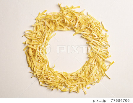 Fresh pasta background. Homemade Italian fettuccine pasta cooked in the home kitchen with fresh eggs and flour on a white light background. Italian food and cuisine concept 77684706