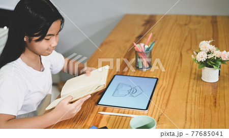 A schoolgirl is doing an E-Learning with a computer tablet at the wooden working desk. A schoolgirl is doing an E-Learning with a computer tablet at the wooden working desk. 77685041