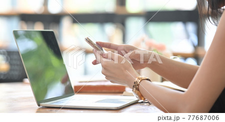 Cropped image of a woman is using a smartphone while sitting in front of a computer laptop. Cropped image of a woman is using a smartphone while sitting in front of a computer laptop. 77687006