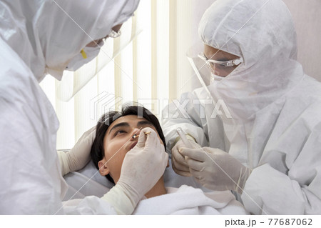 male nurse and doctor wearing ppe suit and facemask perform Coronavirus COVID-19 PCR test. patient nasal NP and oral OP swab sample specimen collection process, viral rt-PCR DNA diagnostic procedure. male nurse and doctor wearing ppe suit and facemask perform Coronavirus COVID-19 PCR test. patient nasal NP and oral OP swab sample specimen collection process, viral rt-PCR DNA diagnostic procedure. 77687062