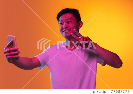Portrait of Asian young man with smartphone isolated over orange yellow background in neon light. 77687277