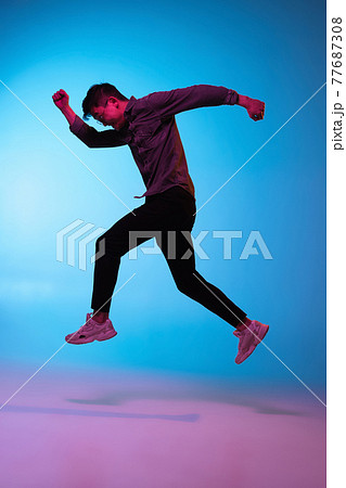 Full length portrait of Asian young man isolated over blue background in neon light 77687308