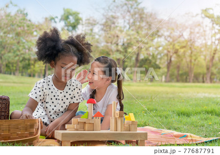 Happy cheerful ethnic girls play wooden block puzzle together at outdoors park , Relationship little kids, Diverse ethnic concept. 77687791