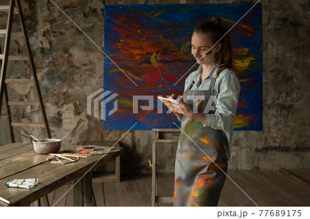 A talented artist using a tablet on the background of a painted picture 77689175