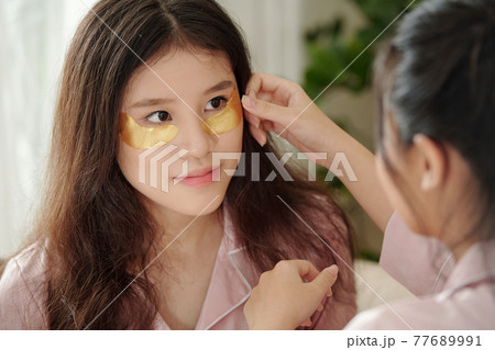 Woman helping friend to apply undereye patches Woman helping friend to apply undereye patches 77689991
