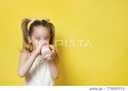 Little girl drinks yogurt from a glass isolated on yellow backdround. Healthy eating concept. Banner with copy space Little girl drinks yogurt from a glass isolated on yellow backdround. Healthy eating concept. Banner with copy space 77690553
