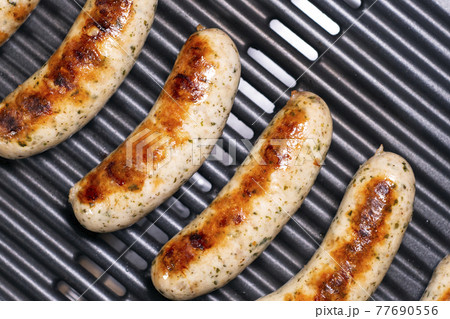 Delicious german sausages on the barbecue electro grill. Tasty sausages sizzling on a portable electric grilling on a summer picnic, close up view. 4k resolution video. 77690556