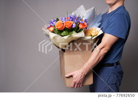 White male courier holding a large cardboard box with several bouquets 77692650