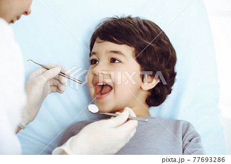 Cute arab boy sitting at dental chair with open mouth during oral checking up with doctor. Visiting dentist office. Stomatology concept Cute arab boy sitting at dental chair with open mouth during oral checking up with doctor. Visiting dentist office. Stomatology concept 77693286