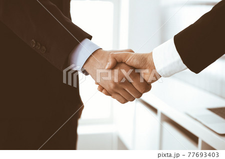 Businessman and woman shaking hands in office. Concept of handshake as success symbol in business Businessman and woman shaking hands in office. Concept of handshake as success symbol in business 77693403