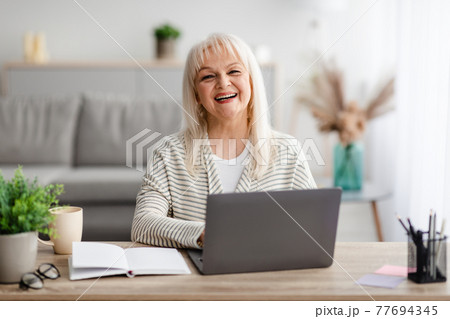 Mature woman sitting at desk and working on computer Mature woman sitting at desk and working on computer 77694345