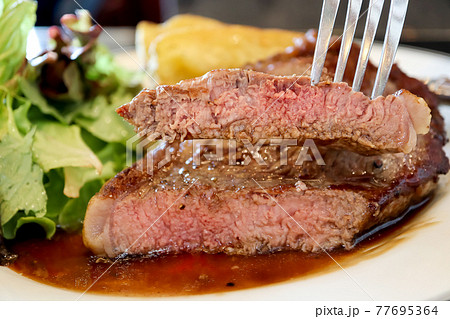 Close-up piece sliced in the fork of sirloin beef steak with brown sauce in white plate background. Medium level ripe. Foods concept. Close-up piece sliced in the fork of sirloin beef steak with brown sauce in white plate background. Medium level ripe. Foods concept. 77695364