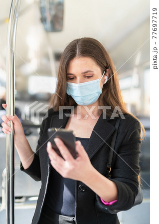 Woman checking her phone while standing on a bus: Selective focus. Safety and new public transport rules concept. 77697719