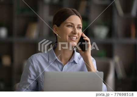 Young female working from home using laptop speaking on telephone 77698518