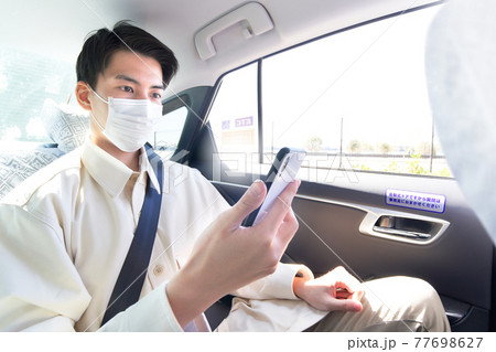 タクシーに乗ってスマホを見るマスク姿の若い男性 タクシーに乗ってスマホを見るマスク姿の若い男性 77698627