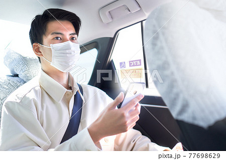 タクシーの後部座席に乗るマスク姿の若い男性 77698629