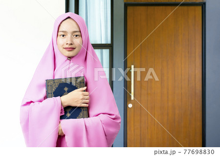 Asian Muslim woman in a veil standing and holding the Quran Asian Muslim woman in a veil standing and holding the Quran 77698830