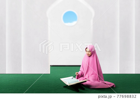 Asian Muslim woman in a veil sitting and reading the Quran Asian Muslim woman in a veil sitting and reading the Quran 77698832