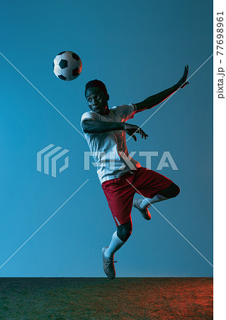 Young African soccer football player posing isolated on blue background in neon light Young African soccer football player posing isolated on blue background in neon light 77698961