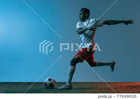 Young African soccer football player posing isolated on blue background in neon light. Rear view 77699030