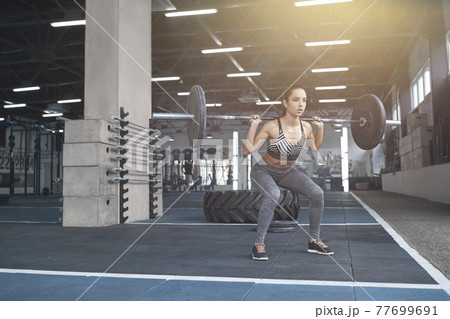 Young woman exercises in gym healthy lifestyle holding barbell close-up 77699691