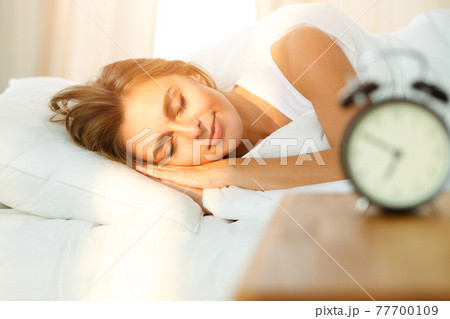 Beautiful blonde girl sleeping sweetly in sunny bedroom on a white bed. Holyday comfort and Rest concepts 77700109