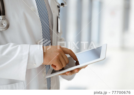 The unknown male doctor is using a tablet computer while standing in a modern clinic, close-up. Medicine concept 77700676