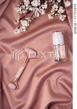 Quartz roller and cometic product on shiny pink fabric. 77701856