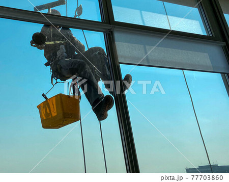 Industrial mountaineering, a man washes the windows of a high-rise building 77703860
