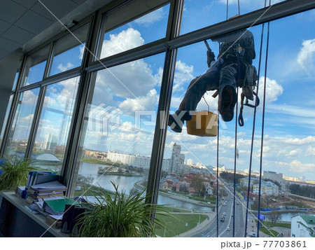 Professional industrial climber in rubber gloves washes windows at high altitude Professional industrial climber in rubber gloves washes windows at high altitude 77703861