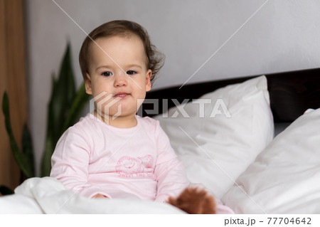 Authentic portrait caucasian little infant chubby baby girl or boy in pink sleepy upon waking looking at camera smiling cute and grimaces in white bed. Child care, Childhood, Parenthood, life concept Authentic portrait caucasian little infant chubby baby girl or boy in pink sleepy upon waking looking at camera smiling cute and grimaces in white bed. Child care, Childhood, Parenthood, life concept 77704642