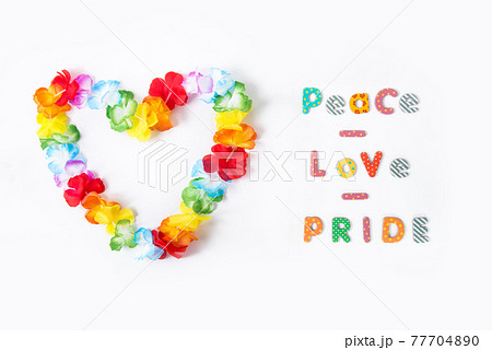 Hawaiian flower necklace in the shape of a heart with Peace Love Pride inscription on the white background. LGBTQ concept with rainbow flag colors. Pride month. Selective focus. Copy space. 77704890