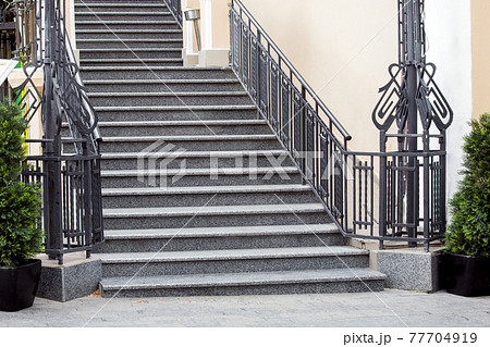 gray granite staircase with stone steps climbing upward with iron railing at the sidewalk from tiles with pots and green thujas cityscape architecture facade, nobody. 77704919