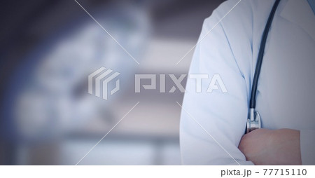 Mid section of male doctor with arms crossed against surgical light in background Mid section of male doctor with arms crossed against surgical light in background 77715110