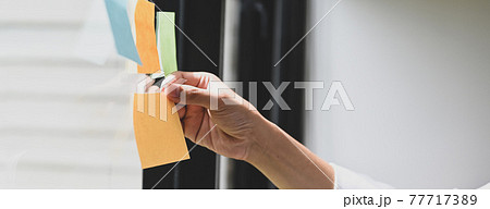 Cropped image a hand is holding an empty sticky note at the glass wall. 77717389