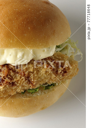 たっぷりのタルタルソースと白身魚のフライがはさまったハンバーガーを白背景で撮影（正面、俯瞰） 77718648