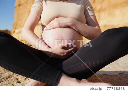 close-up photo. a pregnant woman sits on the seashore 77718848