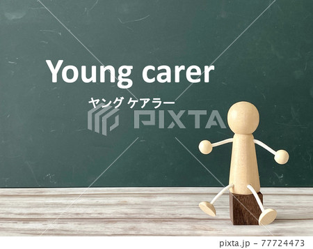 黒板の前の茶色い椅子に座った木の人形_Young carer文字入り 黒板の前の茶色い椅子に座った木の人形_Young carer文字入り 77724473