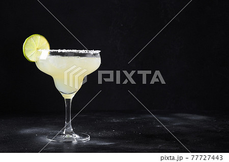 Classic Margarita cocktail with lime juice and ice cube on black background. 77727443