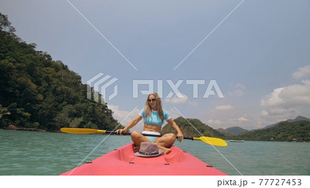 Sportive woman rows pink plastic canoe along sea water. Positive sports girl hand padding on kayak, front view. 77727453