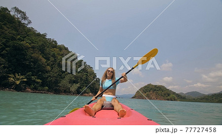 Sportive woman rows pink plastic canoe along sea water. Positive sports girl hand padding on kayak, front view. Sportive woman rows pink plastic canoe along sea water. Positive sports girl hand padding on kayak, front view. 77727458