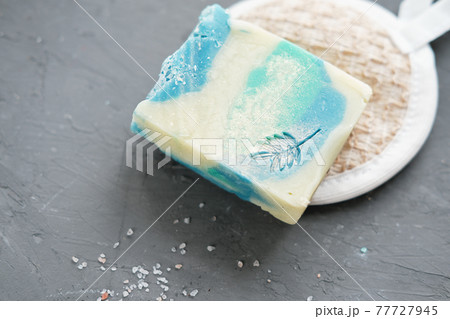 exfoliating sea salt soap bar on a concrete plate and cotton cleansing sponge. sea crystals scattering on a table. hand made craft soap with natural organic oils and skin polishing components exfoliating sea salt soap bar on a concrete plate and cotton cleansing sponge. sea crystals scattering on a table. hand made craft soap with natural organic oils and skin polishing components 77727945