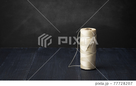 spool of white nylon thread and needle on blue wooden background 77728207