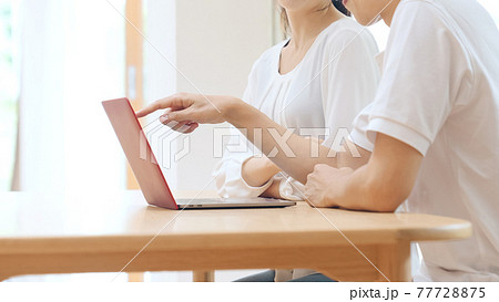 パソコンを見ながら会話するカップル 77728875