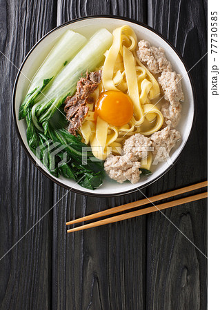 Asian homemade egg noodle soup with anchovies, meatballs and bok choy close-up in a bowl. vertical top view 77730585